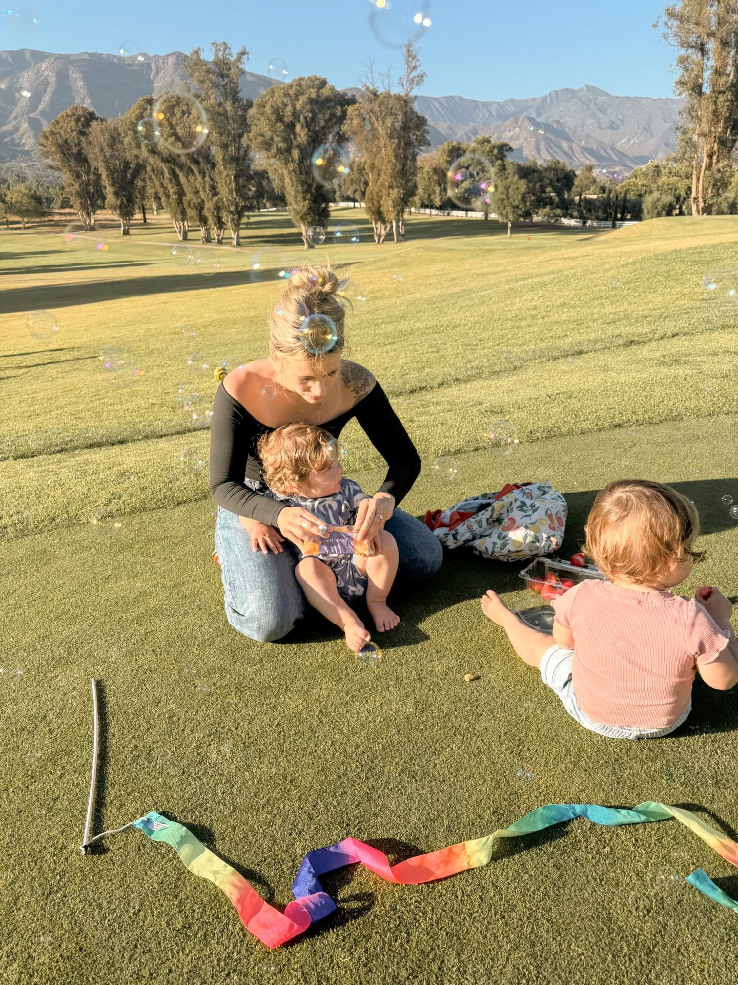 Family with 14-month-old twins playing with bubbles on the lawn at Ojai Valley Inn, with the Topatopa mountains behind