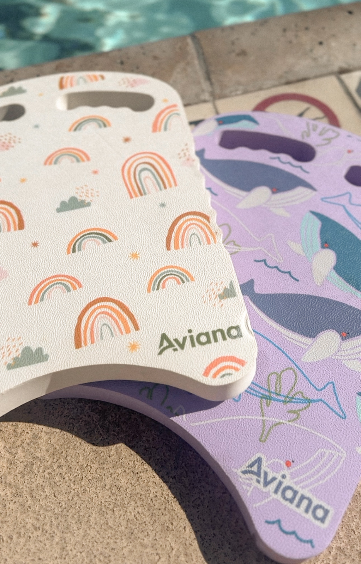 Two personalised swimming kickboards resting on the tiled edge of a pool in bright sun