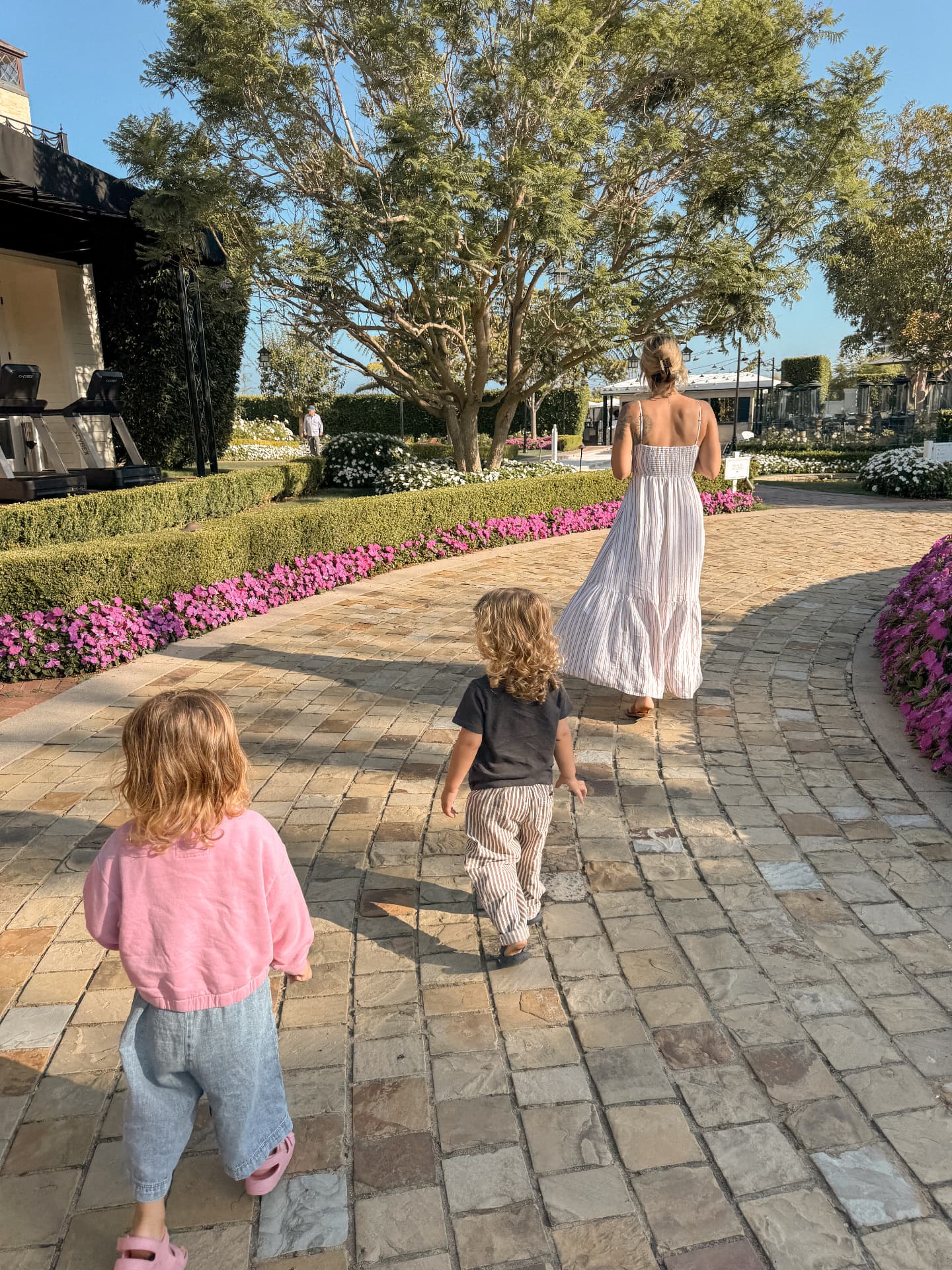 A mother and two small children walking away along a stone path lined with flowers at a coastal resort