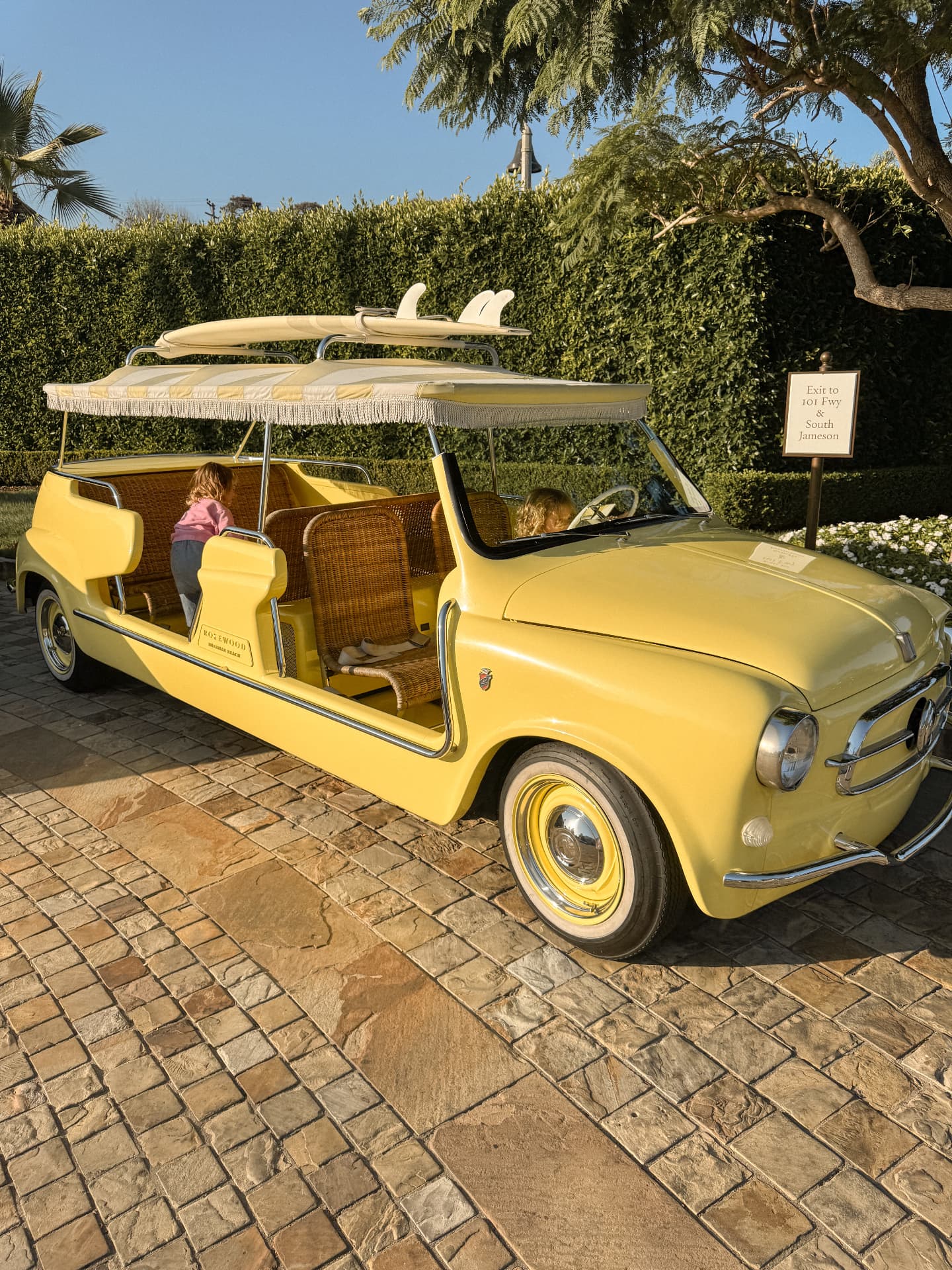 Two small children exploring a yellow vintage resort car with surfboards secured above it